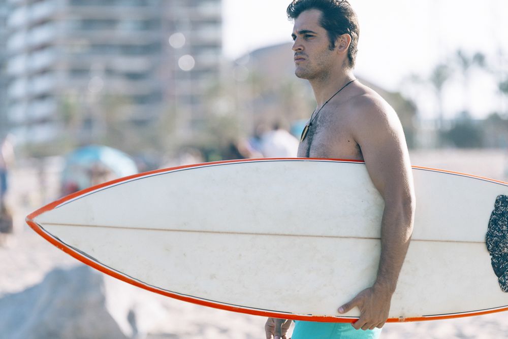 Side view of male surfer walking on beach with board attached to his leg with leash