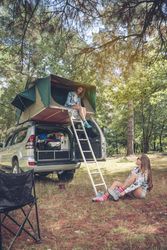 Woman in tent over car getting ready for hike in forest