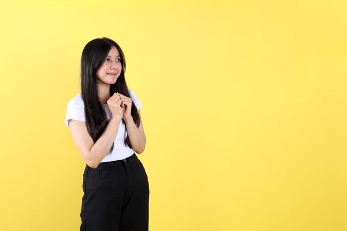Young Asian Indonesian Woman Wearing White Shirt, Her Hands are Clasped in front of Her Chest.