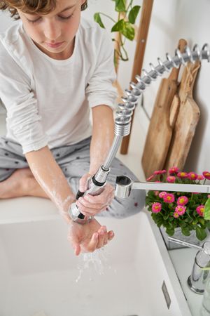 Kid washing soap with water from faucet