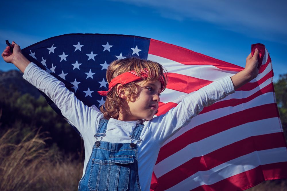 Positive preteen boy with USA waving flag over head