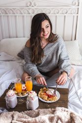 Young woman eating appetizing waffles and tasty drinks on tray on bed