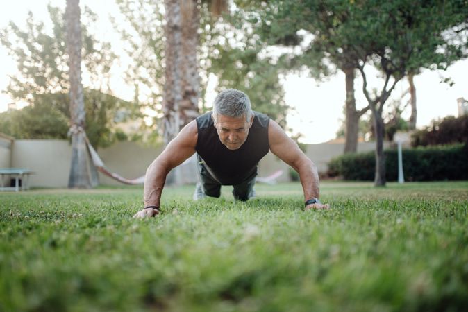 Cheerful older man pushing ups on green grass in park