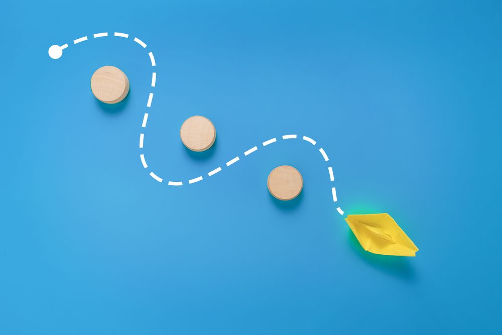 a yellow paper boat passes through barrier. isolated on blue background. concept of avoiding obstacle to achieve a goal