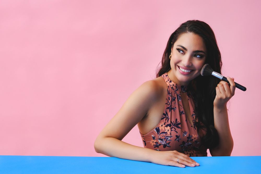 Smiling Hispanic woman with long brown hair holding large make up brush, copy space