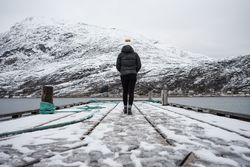 Woman on waterfront against small town at snowy foothill