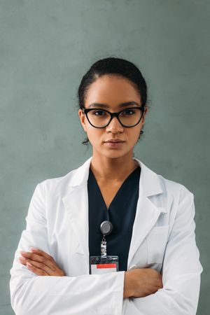 Portrait of young female Black doctor in lab coat in grey room