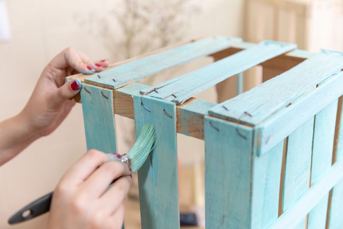 Woman paining wooden box in blue color with brush