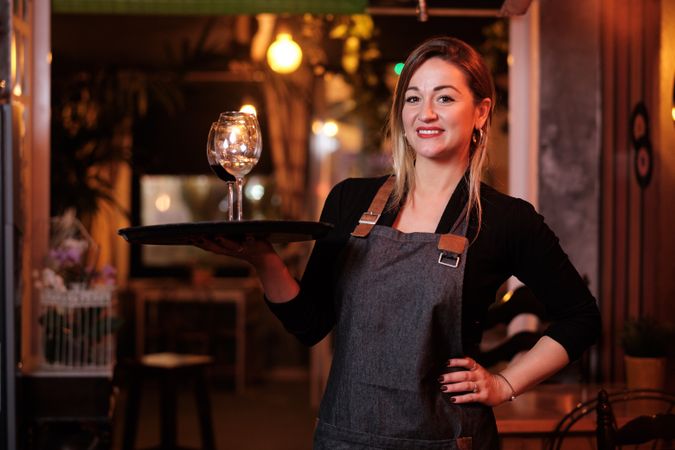 Cheerful waitress holding tray with wineglasses