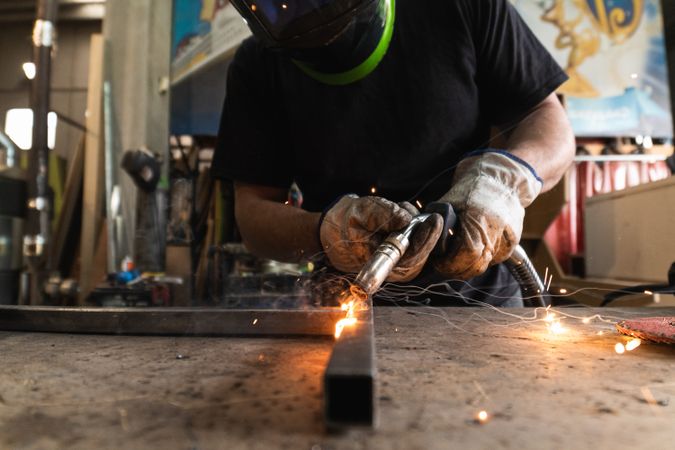 Welder in protective helmet welding metal detail in workshop