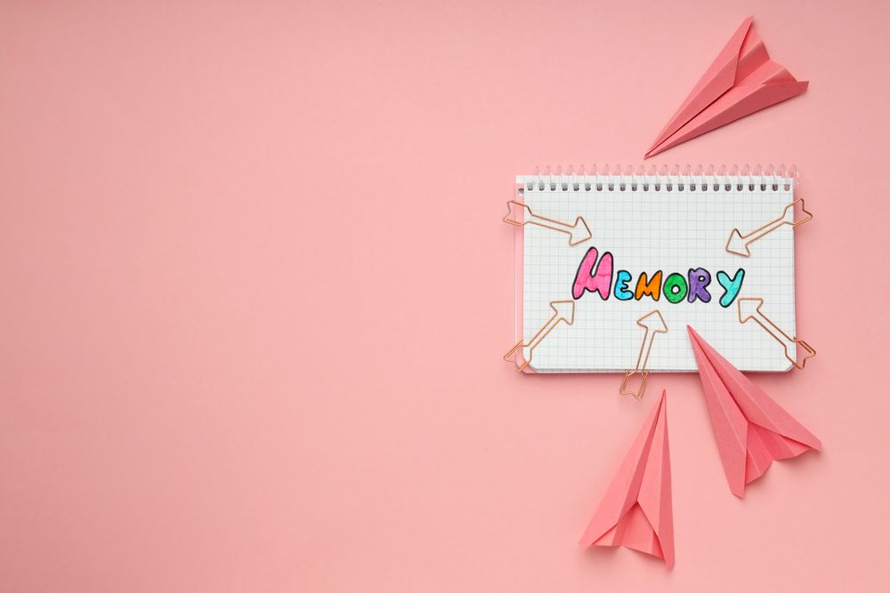 Notepad with “memory” written in colorful markers with paper planes, copy space