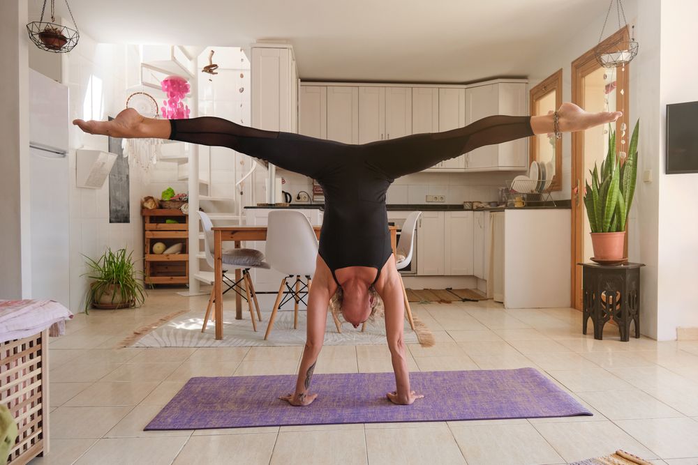 Sportswoman taking Handstand pose with legs apart at home