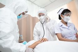 Medical staff in full PPE taking heart rate of patient lying in bed