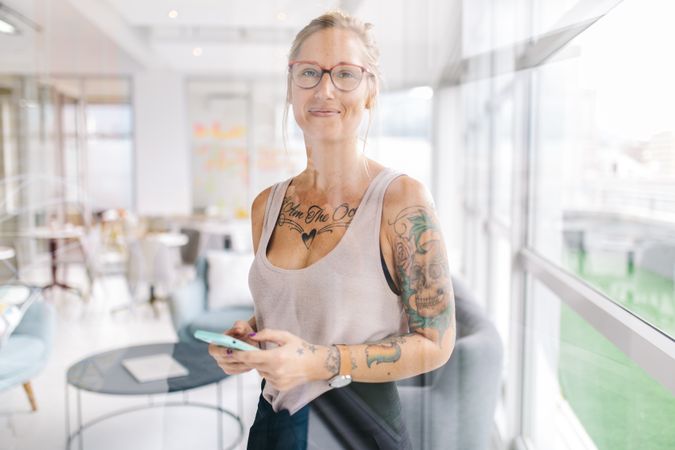 Tattooed woman with smartphone in a bright modern office