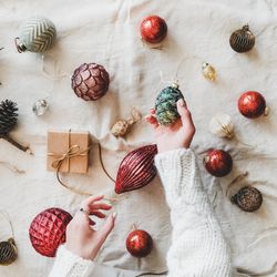 Flat-lay of holiday decoration, with hands holding pinecone top view, square crop