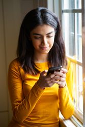 Female texting on phone next to window