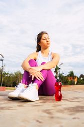 Positive sportswoman with bottle of water sitting on sports ground
