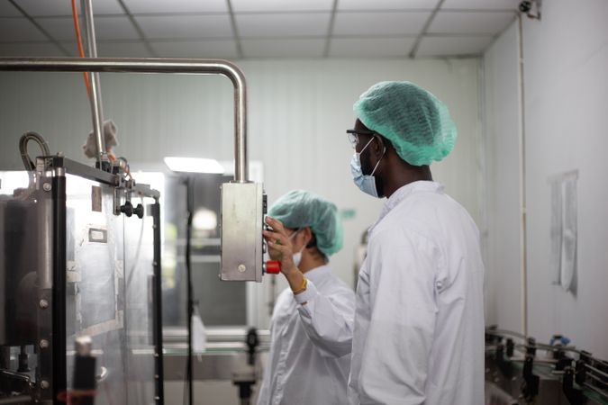 Two diverse factory workers are inspecting machinery inside a beverage production facility.