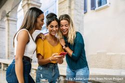 Three female friends looking down and smiling at friends phone 5o8xG4