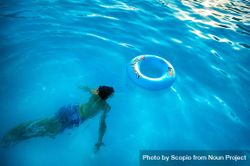 Person swimming underwater near inflatable ring in swimming pool 5lK9v0