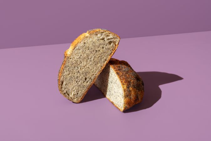 Bread with poppy seeds sliced in half, isolated on a purple background