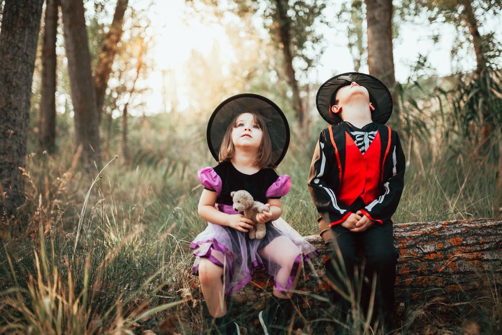 Brother and sister in halloween costumes looking up at the sky from the forest