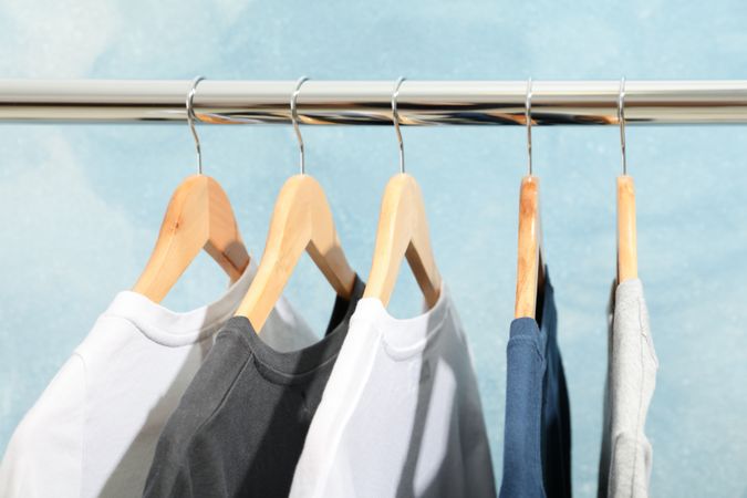 Rack with blank t-shirts on blue background, close up