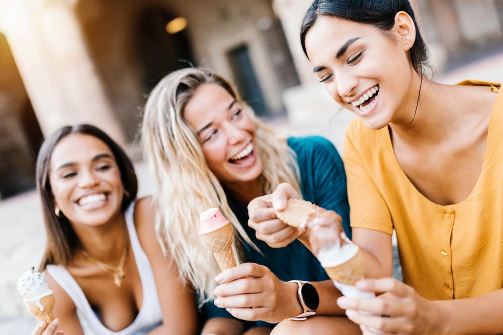 Happy multi-ethnic women laughing together outdoors while eating ice cream