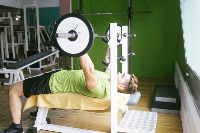 Side view of man in green t-shirt lifting heavy bar exercising chest