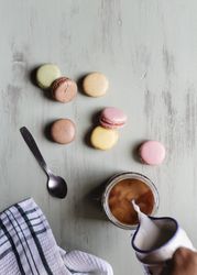 Crop person adding milk to coffee near macaroons