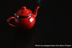 Enamel red tea pot on dark table with steam rising from spout 5wlW94
