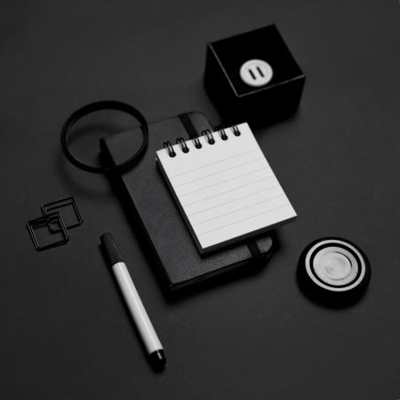 Monochrome photo of small notebook and office stationary on dark table