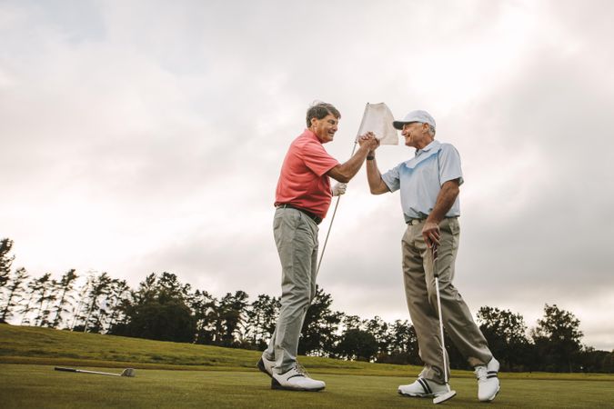 Two older friends shaking hands at golf course after end of round