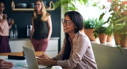 Woman smiling at laptop surrounded by colleagues