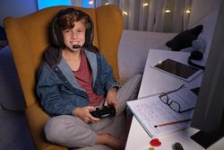 Child in headset enjoying game on computer in dark room