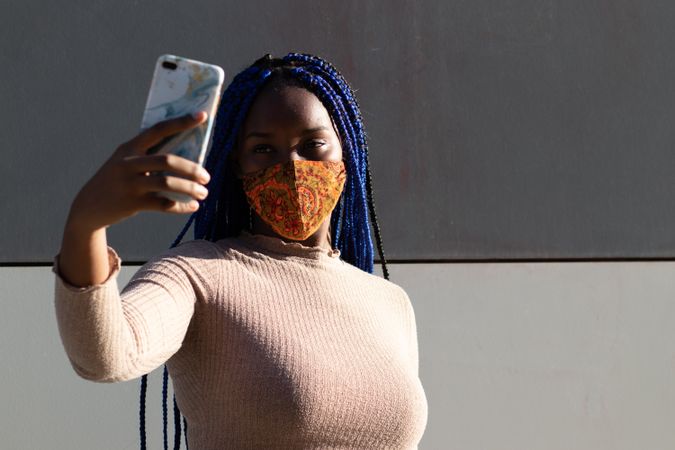 Stylish Black woman taking selfie in mask