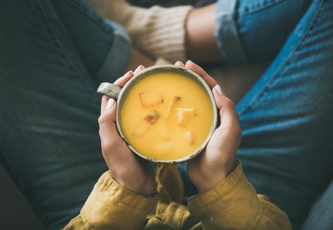 Woman in jeans holding cup of squash soup