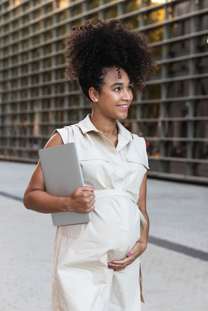 Smiling Black woman with laptop coming out of office building