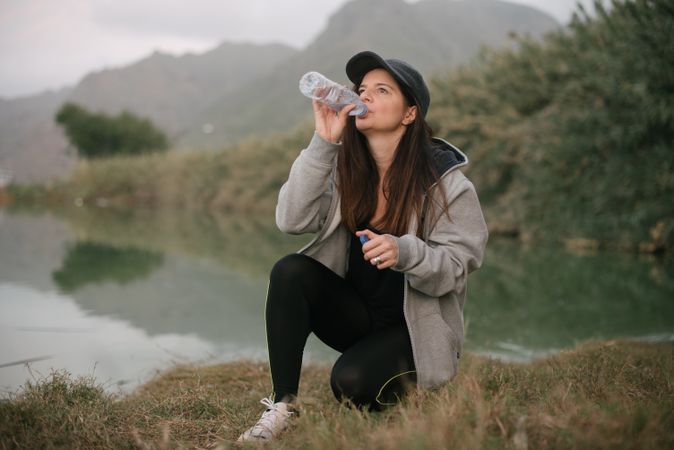 Woman drinking water near lake between mountains