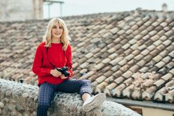 Smiling woman sitting on rocky stoop in Spanish town with SLR camera