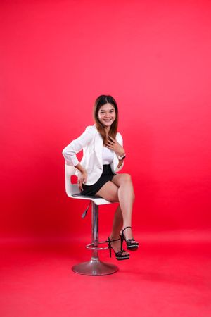 Full length young woman wearing a cheerful suit, sitting on a hydraulic chair isolated on a red background