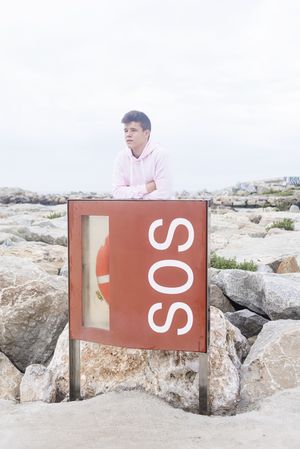 Young male teenager with arms crossed standing on promenade by emergency life jacket