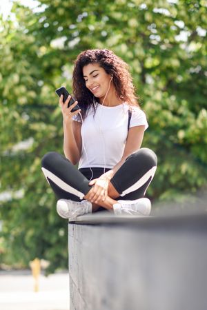 Arab woman smiling while using phone sitting outdoors, vertical