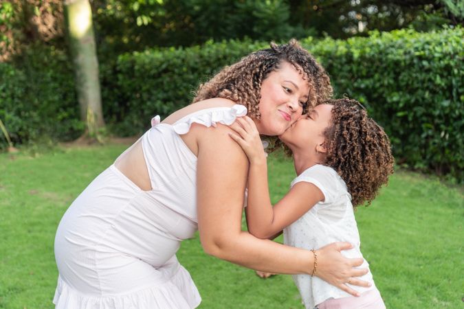 A girl kisses her mother on the cheek in the open air