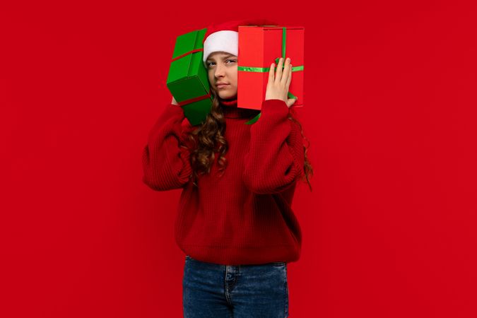 Girl in Santa hat holds Christmas presents to her ears
