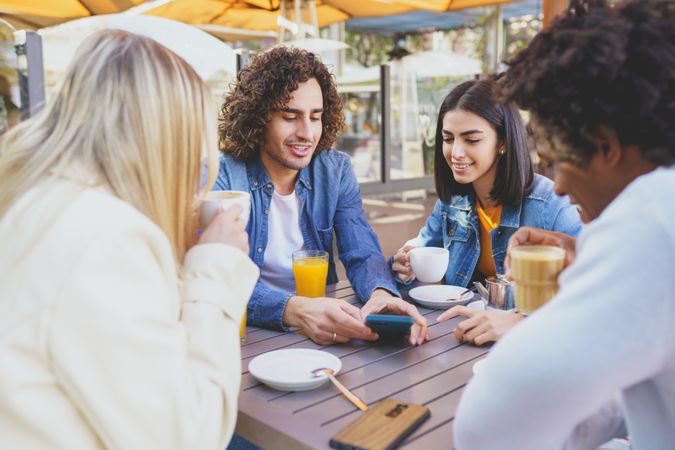 Friends looking at phone of male over coffee and juice outside