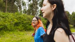Two friends walk happily, chatting, during an excursion to a beach in Galicia, green trees can be seen in the background