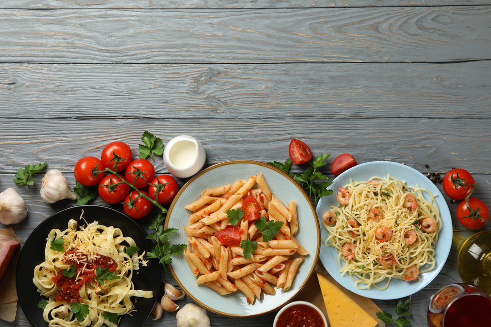 Composition with plate of tasty pasta and ingredients for cooking on wooden background