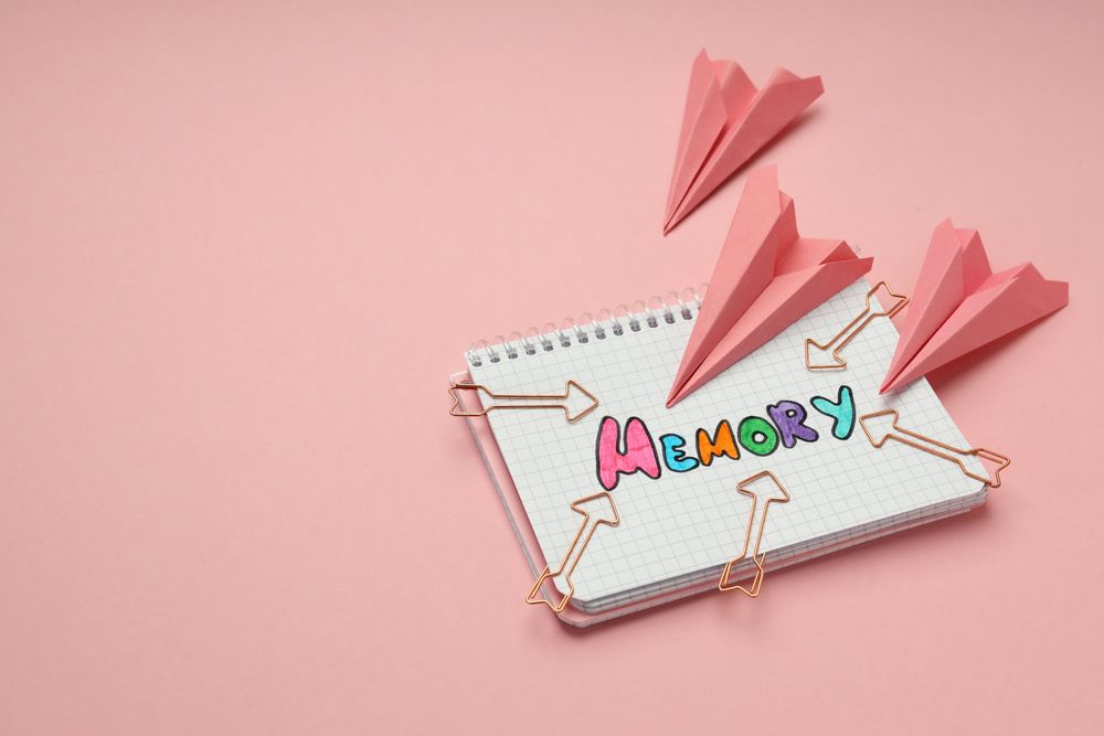 Notepad with “memory” written in colorful markers with arrow shaped paper planes, copy space