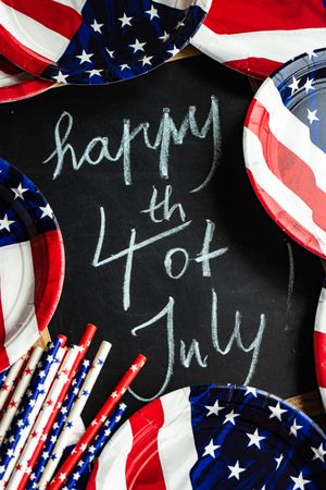 Chalkboard surrounded by American flag tableware with the words "Happy 4th of July"